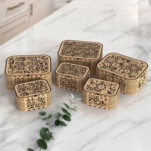 Könnte beinhalten: Fünf Holzkisten mit aufwendigen Blumendesigns. Die Kisten sind ineinander verschachtelt, wobei die größte Kiste unten und die kleinste oben liegt. Die Kisten sind aus hellbraunem Holz gefertigt und haben eine natürliche Oberfläche.