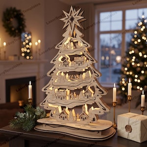 May include: A laser-cut wooden Christmas tree decoration featuring a multi-layered winter village scene with houses, trees, and figures. The tree is topped with a star and illuminated from within, resting on a tiered oval wooden base.