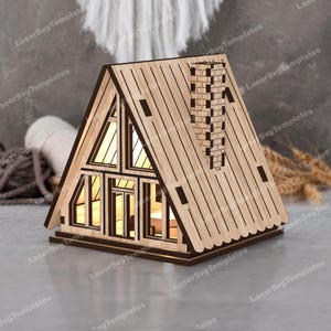 May include: A wooden model of a cabin with a chimney and windows. The cabin is made of light brown wood and has a dark brown roof. The windows are clear and the chimney is made of dark brown bricks.