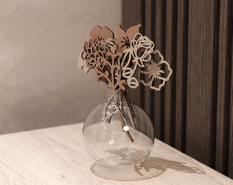 May include: A clear glass vase with a round base holds a bouquet of brown and beige wooden flowers. The flowers are cut out in the shape of various blooms and leaves.