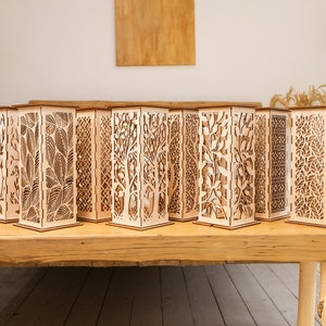 Pode incluir: Um conjunto de 10 l&acirc;mpadas decorativas de madeira com designs intrincados cortados a laser. Cada l&acirc;mpada apresenta um padr&atilde;o diferente de folhas, galhos e formas geom&eacute;tricas. As l&acirc;mpadas s&atilde;o feitas de madeira natural e t&ecirc;m uma est&eacute;tica quente e r&uacute;stica.