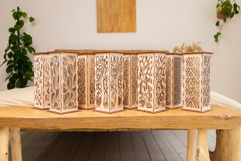 Pode incluir: Um conjunto de 10 l&acirc;mpadas decorativas de madeira com designs intrincados cortados a laser. Cada l&acirc;mpada apresenta um padr&atilde;o diferente de folhas, galhos e formas geom&eacute;tricas. As l&acirc;mpadas s&atilde;o feitas de madeira natural e t&ecirc;m uma est&eacute;tica quente e r&uacute;stica.