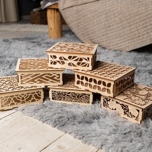 May include: Six wooden boxes with intricate laser cut designs. The boxes are stacked on top of each other on a gray fluffy rug.