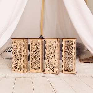 Pode incluir: Quatro lanternas decorativas de madeira com designs intrincados cortados a laser. As lanternas est&atilde;o dispostas em fila sobre um tapete de pele sint&eacute;tica branca.
