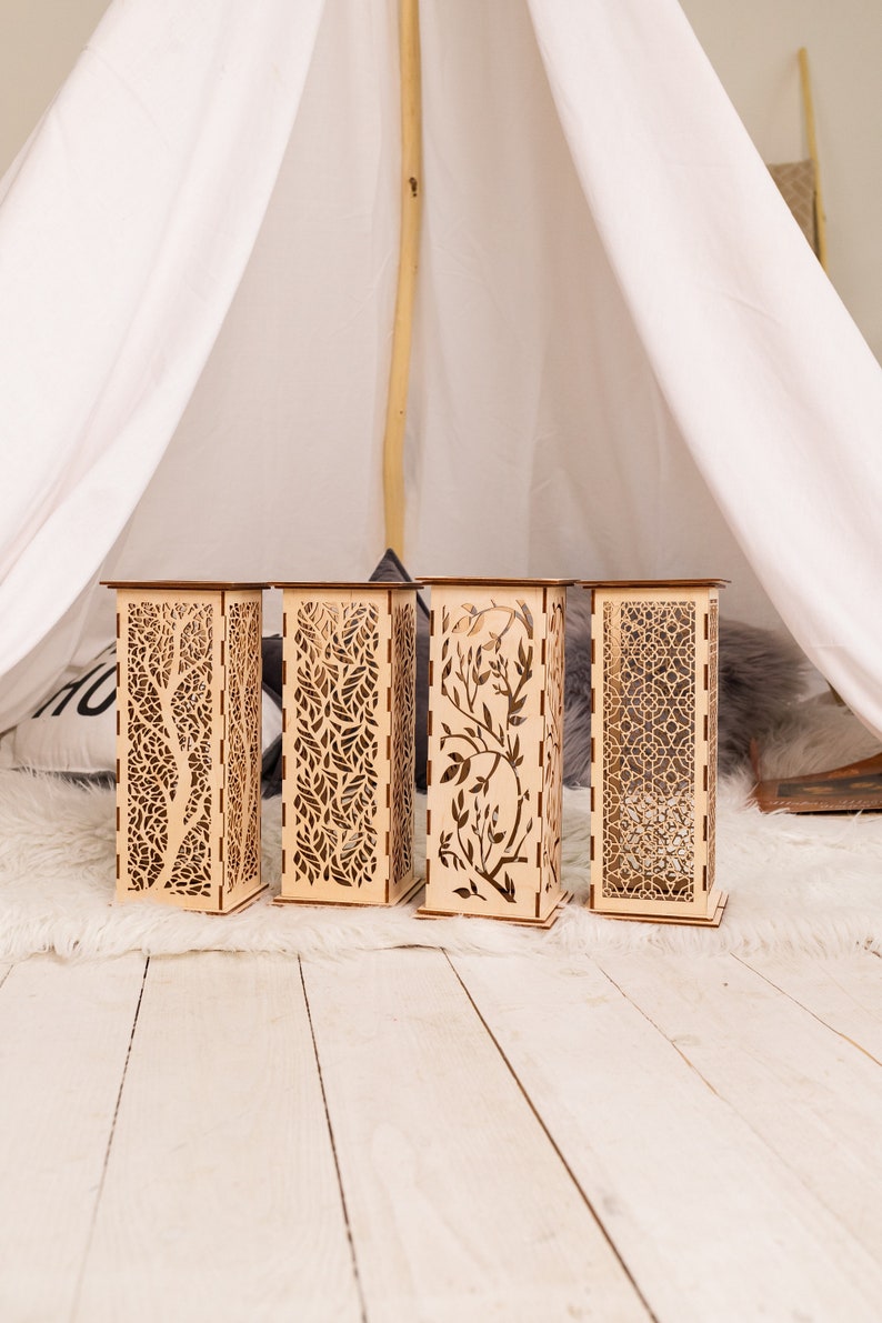 Pode incluir: Quatro lanternas decorativas de madeira com designs intrincados cortados a laser. As lanternas est&atilde;o dispostas em fila sobre um tapete de pele sint&eacute;tica branca.