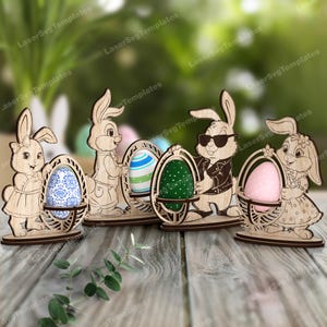 Op de afbeelding: Houten paashaasfiguren die decoratieve eieren vasthouden. De konijnen hebben verschillende poses en outfits. De eieren zijn beschilderd met verschillende patronen en kleuren, waaronder blauw, groen en roze.