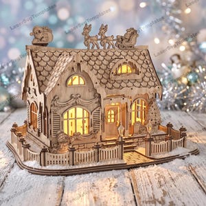 May include: A light-colored wooden model house featuring laser-cut details including a snowman, a Christmas tree, and a sleigh with reindeer on the roof. The structure has arched windows, a shingled roof, and a picket fence, all illuminated from within.