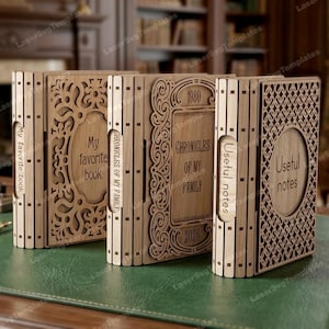 Puede incluir: Una colección de cajas de madera con forma de libro con intrincados diseños cortados con láser. Las cajas presentan textos como "My favorite book", "Chronicles of my family" y "Useful notes". Las cajas son de madera clara y se exhiben sobre una superficie verde.