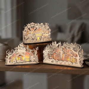 May include: Three layered wooden Halloween decorations with intricate laser-cut designs. The pieces feature scenes of a carnival, a haunted house, and a graveyard, all illuminated from within by warm light, showcasing pumpkins, trees, and ghosts.