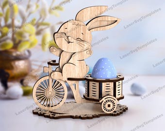 May include: Wooden Easter egg holder featuring a bunny riding a bicycle. The holder has a blue egg with white polka dots and a basket for additional eggs.