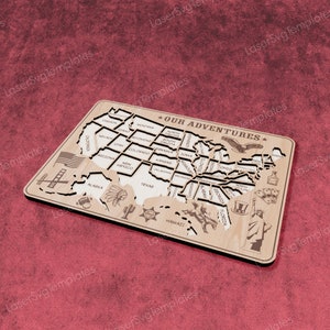 May include: A wooden map of the United States with each state outlined and labeled. The map is designed to be a puzzle with each state a separate piece. The map is decorated with icons representing each state, such as a cowboy hat for Texas, a palm tree for Florida, and a Statue of Liberty for New York. The map is titled "Our Adventures".