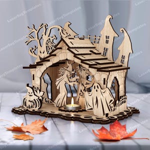 Könnte beinhalten: Ein hölzernes Halloween-Dekorationshaus mit Ausschnitten einer Hexe, eines Geistes und eines Kürbisses. Das Laser-Design umfasst einen Baum, ein Spinnennetz und einen Kerzenhalter. Das Haus ist aus hellem Holz gefertigt und hat ein detailliertes Dach.