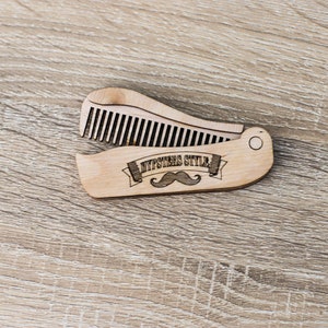 Op de afbeelding: Een houten kam met een vouwbaar ontwerp. De kam heeft een snor en de tekst "Hipsters Style" gegraveerd.