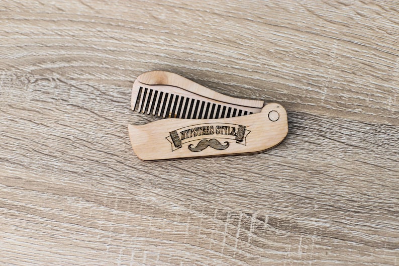 Op de afbeelding: Een houten kam met een vouwbaar ontwerp. De kam heeft een snor en de tekst "Hipsters Style" gegraveerd.