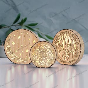 May include: Three wooden laser cut nightlight designs. The first design features a crescent moon and stars. The second design features a mandala. The third design features a floral pattern.