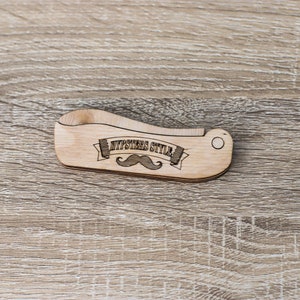 Op de afbeelding: Een houten kam met een gebogen handvat en een snorontwerp. De kam is gegraveerd met de woorden "Hipsters Style".