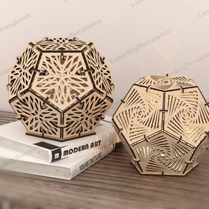May include: Two wooden geometric lamps with intricate laser cut designs. The lamps are on a wooden surface with a book titled "Modern Art" visible.