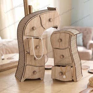 May include: Two wooden jewelry boxes with curved designs and multiple drawers. The larger box has a pearl necklace hanging from a drawer, while the smaller box has a gold necklace with a pendant. The boxes are on a light-colored wooden surface.