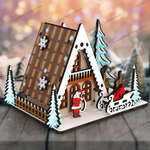 May include: A wooden Christmas house with a brown roof, white trim, and a Santa Claus figure standing in front. The house has a fence and two small trees on either side. There is a sleigh with a red bag in front of the house.