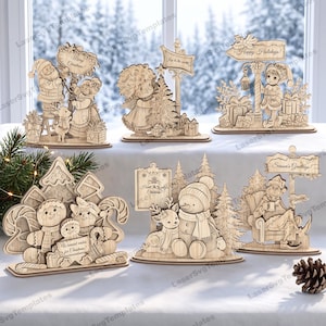May include: A collection of six laser-cut wooden Christmas ornaments featuring various holiday scenes. Designs include Santa, an angel, an elf, gingerbread figures, a snowman with a reindeer, and a character in a chair, all with engraved text.