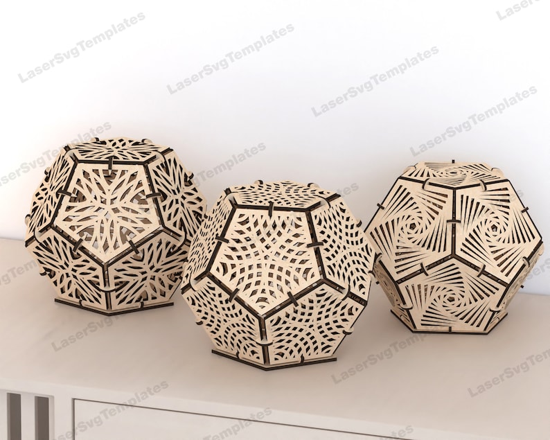 May include: Three wooden geometric lampshades with intricate laser cut designs. The lampshades are in the shape of a dodecahedron and are made of light brown wood.