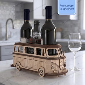 Op de afbeelding: Een lichtgekleurde houten flessenhouder in de vorm van een vintage busje, met twee wijnflessen en één sterke drankfles. De structuur heeft lasergesneden details zoals wielen, ramen en bumpers. Een blauw bordje vermeldt Instruction is included.