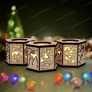 Op de afbeelding: Drie zeshoekige houten kaarshouders met ingewikkelde uitsnijdingen die de kerststal voorstellen. De houders zijn van binnenuit verlicht, waardoor een warm gloed ontstaat.