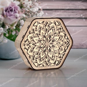 Puede incluir: Una lámpara hexagonal de madera con un diseño floral en capas. La lámpara está hecha de madera de color claro y presenta intrincados patrones recortados que crean un hermoso efecto de luz. Es un artículo de decoración del hogar.