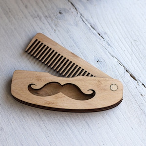 May include: A wooden comb with a moustache cutout design. The comb is folded closed and has a small metal rivet.
