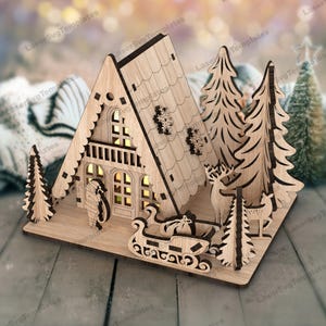 May include: A wooden laser cut Christmas scene with a small house, two trees, a deer, and a sleigh with a bag of gifts. The house has windows and a door, and the trees have branches and needles. The deer is standing in the snow, and the sleigh is filled with gifts.