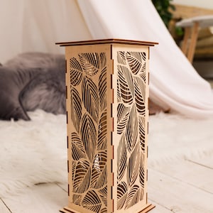 Pode incluir: Uma l&acirc;mpada de madeira com um design de folhas. A l&acirc;mpada &eacute; feita de madeira marrom claro e tem uma base quadrada. As folhas s&atilde;o cortadas na madeira e criam um padr&atilde;o delicado.