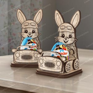 Puede incluir: Dos soportes de coche de conejito de Pascua de madera, cada uno con un conejito con gafas y sosteniendo un huevo Kinder Sorpresa. Los coches tienen ruedas detalladas y una parrilla delantera. El diseño está cortado con láser.