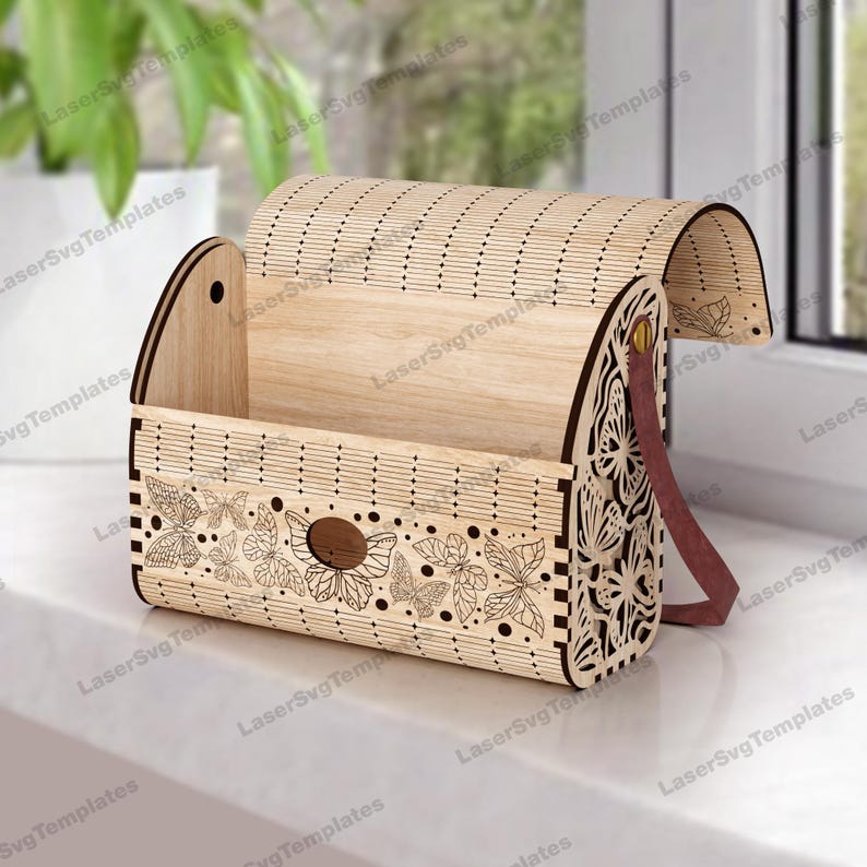 May include: A wooden box with a hinged lid and a leather strap. The box is decorated with a laser-cut design of butterflies. The box is open and the inside is visible.