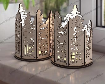 Puede incluir: Dos portavelas de madera con un diseño de bosque cortado con láser. Los portavelas son cilíndricos y tienen un acabado marrón oscuro.
