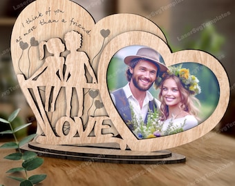May include: Wooden heart-shaped picture frame with two cut-out silhouettes of people holding hands. The frame has the words "I think of you as more than a friend." and "LOVE" carved into it. The frame is designed to hold two photos, one in each heart.