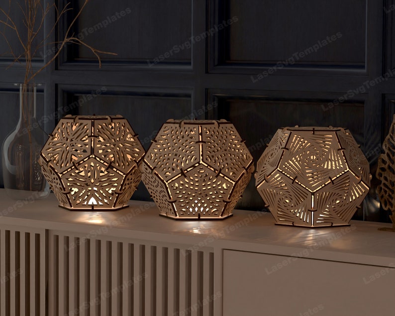 May include: Three wooden geometric lamps with intricate cut-out designs. The lamps are illuminated from within, casting a warm glow. The lamps are arranged on a wooden shelf with a slatted front.