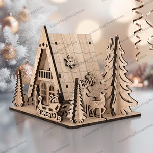 May include: A wooden Christmas village scene with a gingerbread house, two pine trees, and a reindeer pulling a sleigh. The house has a white snowflake on the roof and a balcony. The sleigh is filled with presents.