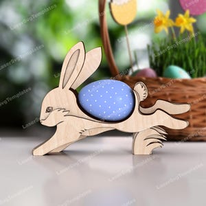 May include: A wooden bunny rabbit cutout holding a blue and white polka dot Easter egg. The bunny is running and has a fluffy tail.