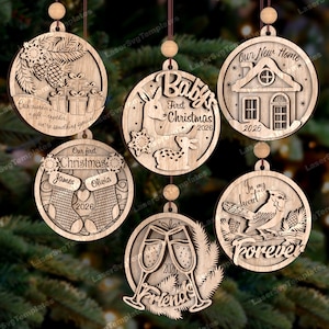 Op de afbeelding: Houten kerstversieringen met diverse ontwerpen. Eén heeft cadeaus en tekst, een ander een hert en een sneeuwvlok, en een derde een huis. Andere ornamenten zijn kousen, champagneglazen en een vogel.