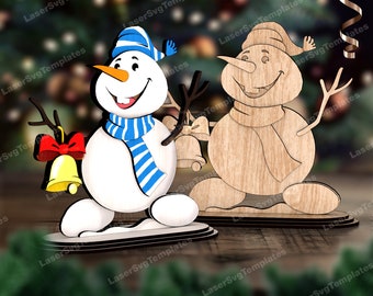 May include: Two snowman figurines. One is painted white with a blue and white striped scarf and hat, a carrot nose, and a red bow with a gold bell. The other is made of wood with a scarf and hat.