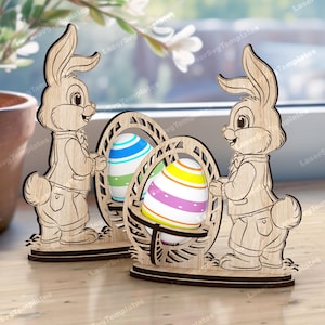 Könnte beinhalten: Zwei hölzerne Osterhasen-Figuren, die Körbe mit Eiern halten. Die Hasen sind hellbraun, die Eier sind bunt gestreift. Ideal für Osterdekorationen und Frühlingsfeiern.