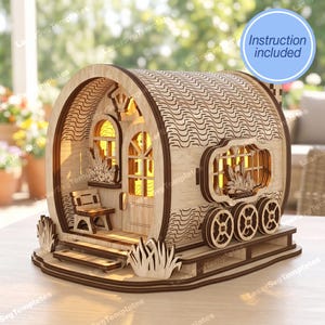 May include: A wooden laser-cut miniature caravan with intricate details. The model features arched windows, a small chair, and decorative wheels. The text "Instruction included" is visible. The caravan is made of light brown wood.