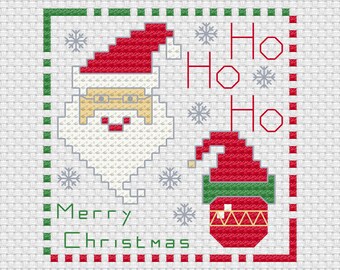 Op de afbeelding: Een kruissteekpatroon op witte stof met een gepixeld gezicht van de Kerstman, een rood-groene elfenmuts en de tekst "Ho Ho Ho" en "Merry Christmas" in rood en groen. Het ontwerp is omlijst door een rand van afwisselend rode en groene vierkantjes.