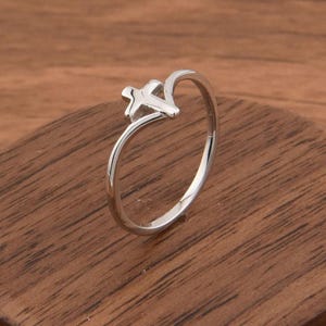 May include: A silver ring featuring the outline of the state of Texas. The ring is displayed on a round, dark wooden stand. The ring's design is simple and elegant, with a polished finish.