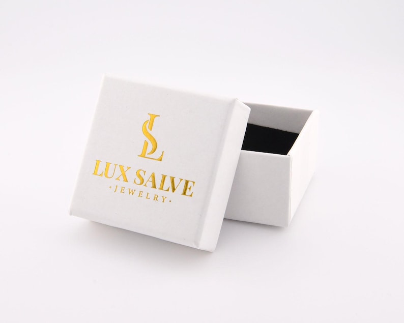May include: A white jewellery box with the text "LUX SALVE JEWELRY" in gold lettering. The box is open, revealing a black interior. The box is on a white surface.