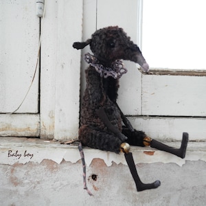 May include: A black and gray plush toy with a long snout and a purple lace collar sits on a white windowsill. The toy has long, black legs and a long, black tail. The text "Baby boy" is written on the windowsill.