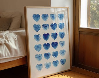 May include: A framed art print featuring a collection of blue watercolor hearts arranged in rows. The hearts vary in shade and texture, creating a visually appealing pattern. The artwork is displayed in a light-colored wooden frame, leaning against a wall.