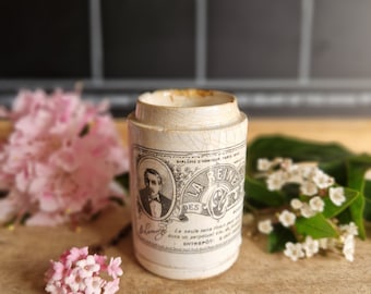 May include: A vintage ceramic jar with a chipped white glaze and a black and white label that reads "La Reine des Blemy" with a portrait of a man in a suit and bow tie. The label also includes the text "Diplome d'Honneur Paris" and "La seule sans rouille", and "Entrepôt S. Just."