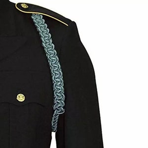 K&ouml;nnte beinhalten: Nahaufnahme einer schwarzen Milit&auml;runiformjacke mit einer hellblauen Schulterschnur. Die Jacke hat goldfarbene Akzente auf der Schulter und einen goldenen Knopf. Die Schulterschnur ist ein geflochtenes Design.