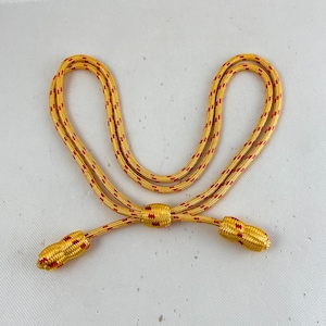 May include: A yellow and red braided cord with two tassel ends. The cord is used for a uniform or ceremonial attire.